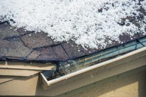 Snow-covered roof and gutters of a house. White snow on dark shingles and a cream-colored gutter.
