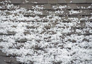 White hailstones covering a gray asphalt shingle roof.
