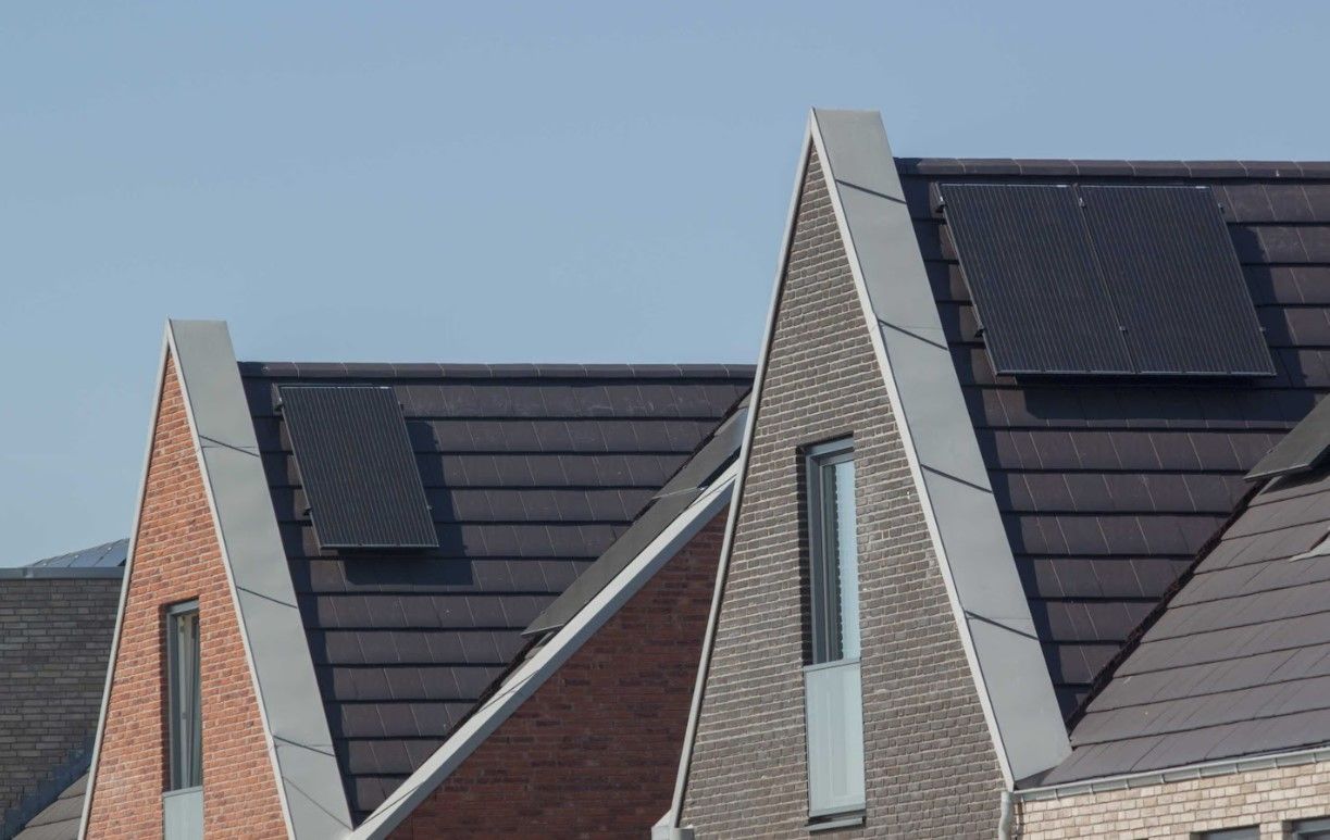 Row of houses with angled roofs, some with solar panels. Clear blue sky.