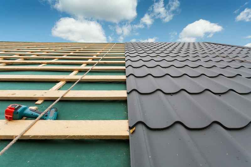 Roof partially covered in dark metal tiles; other side shows wood beams and underlayment.