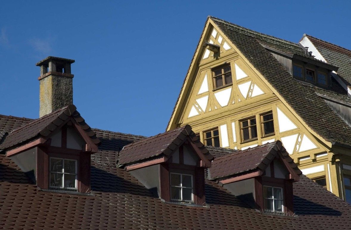 Roofs of timber-framed buildings with dormer windows against a blue sky.