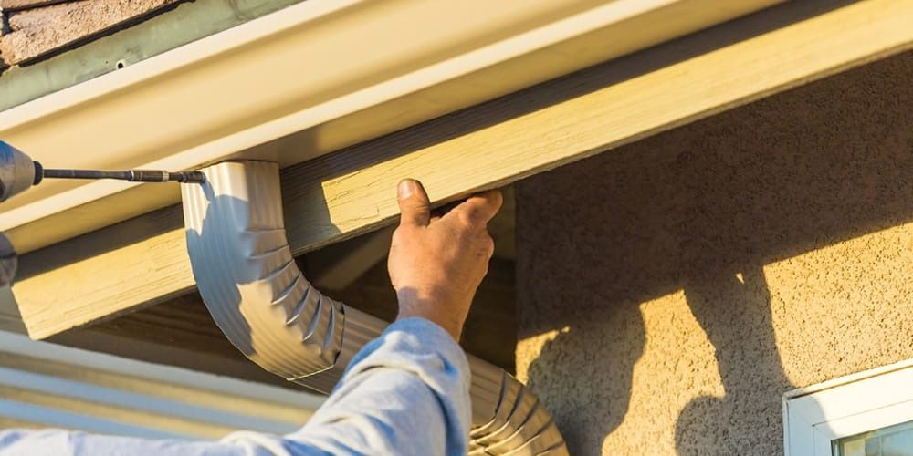 Person installing a gutter downspout using a drill.