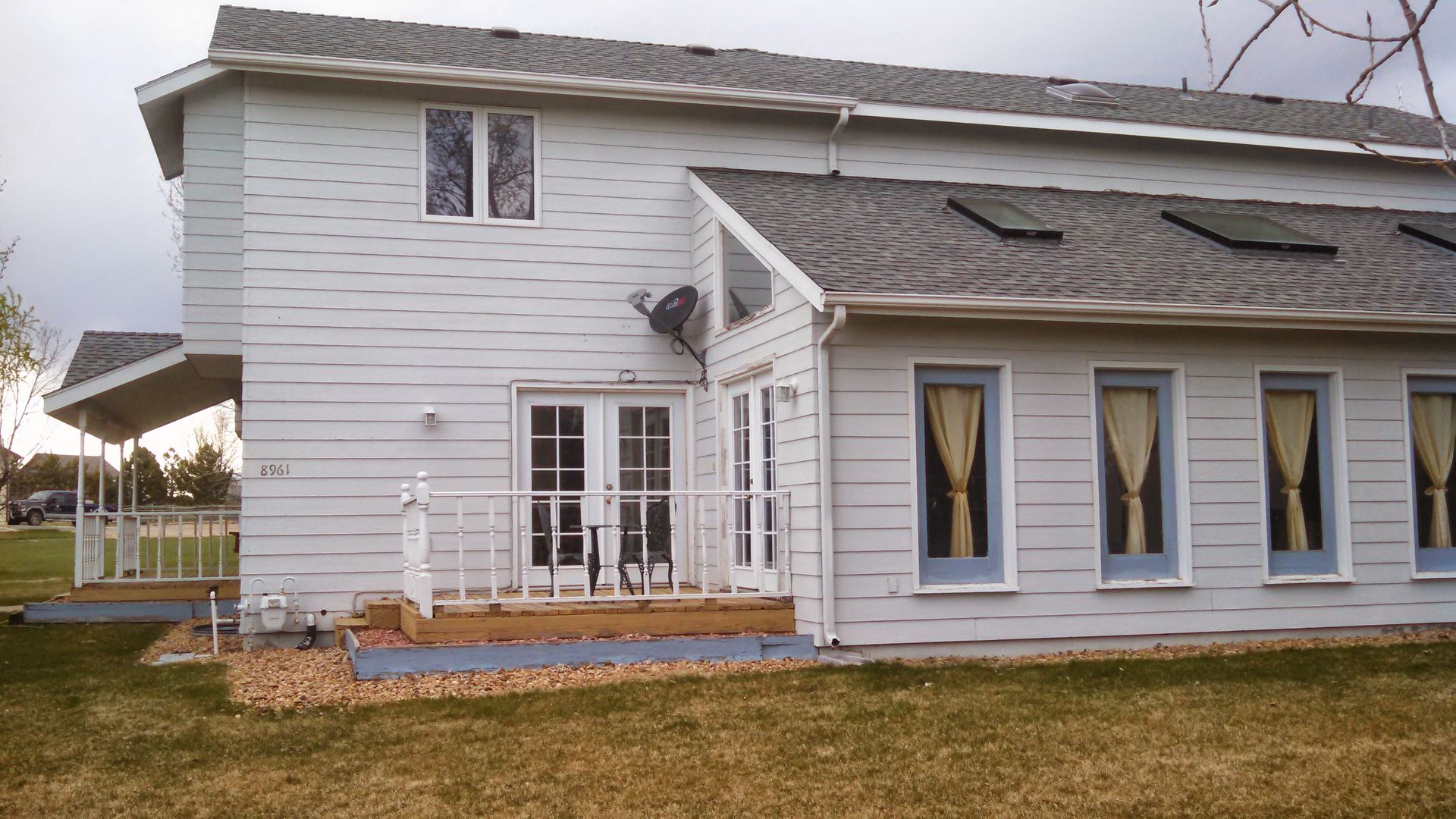 White two-story house with blue siding, porch, and decorative windows on a grassy lawn
