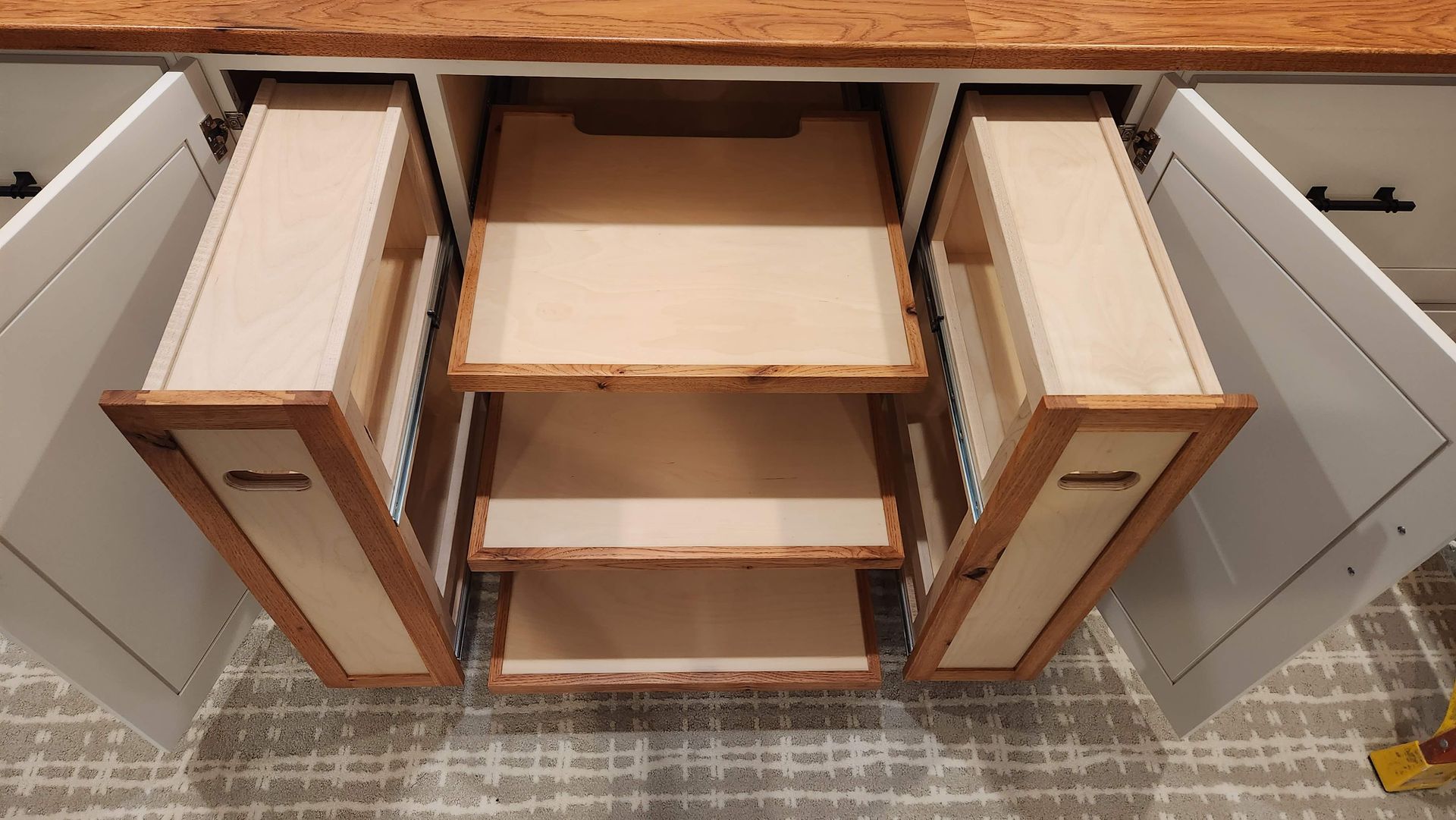 Open cabinet with two wooden pull-out drawer organizers in a kitchen or bathroom vanity.