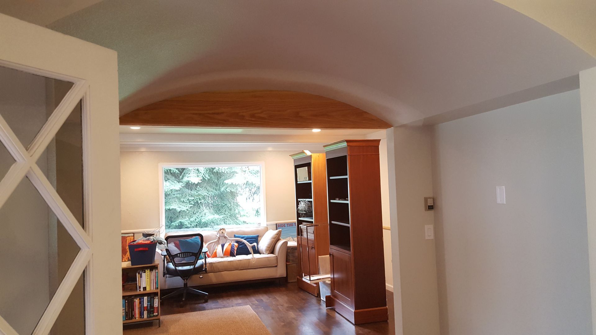 Modern living room with arched ceiling, wood floor, sofa by window, and open shelving.