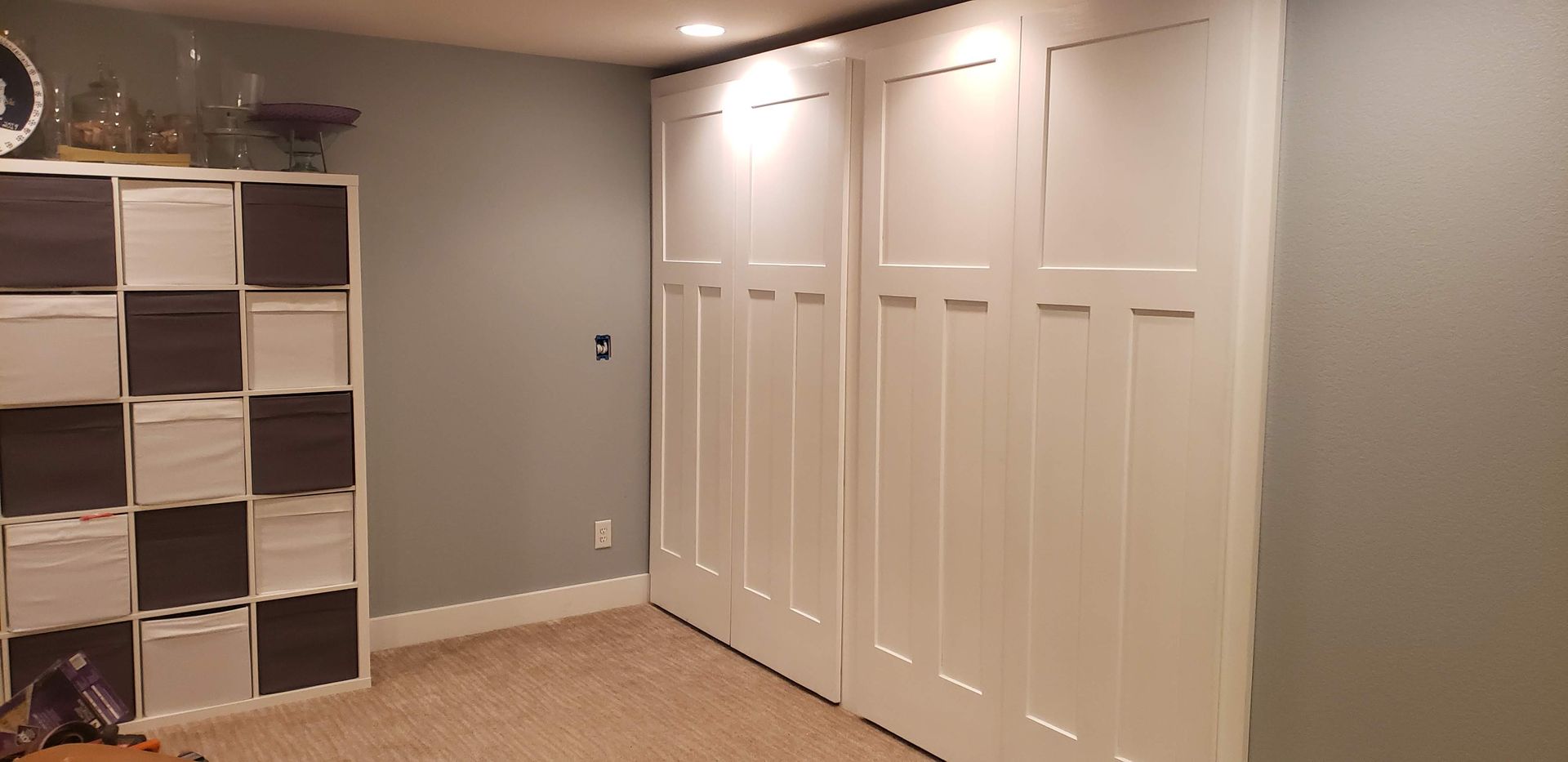Basement room with beige carpet, white closet doors, and a gray wall with cube shelving.