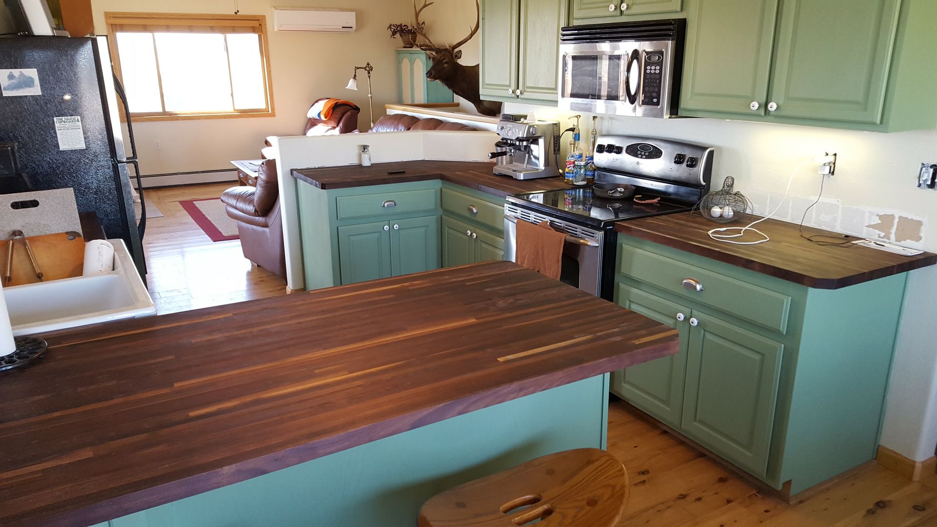 Small kitchen with green cabinets, wood floors, a center island, stove, sink, and refrigerator.
