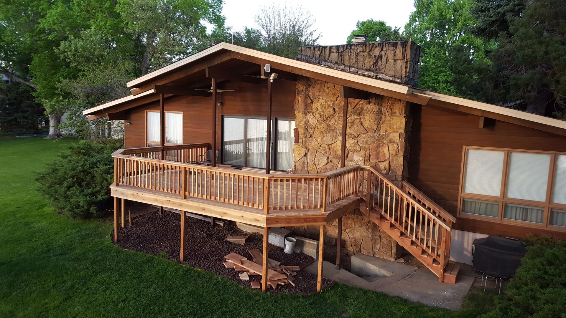 Wooden cabin with porch and stairs on a grassy hillside, surrounded by trees.