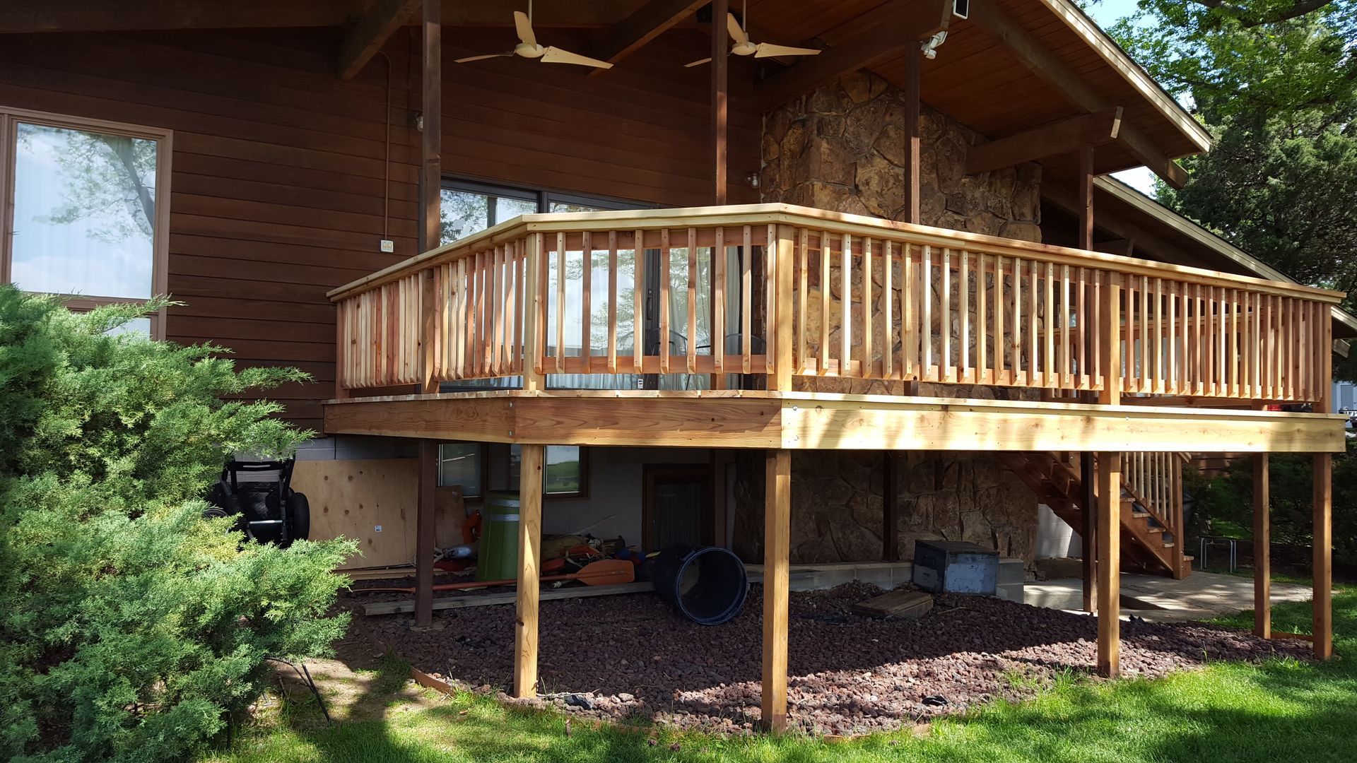 Wooden cabin with an elevated deck and railing, set in a grassy yard with trees nearby.