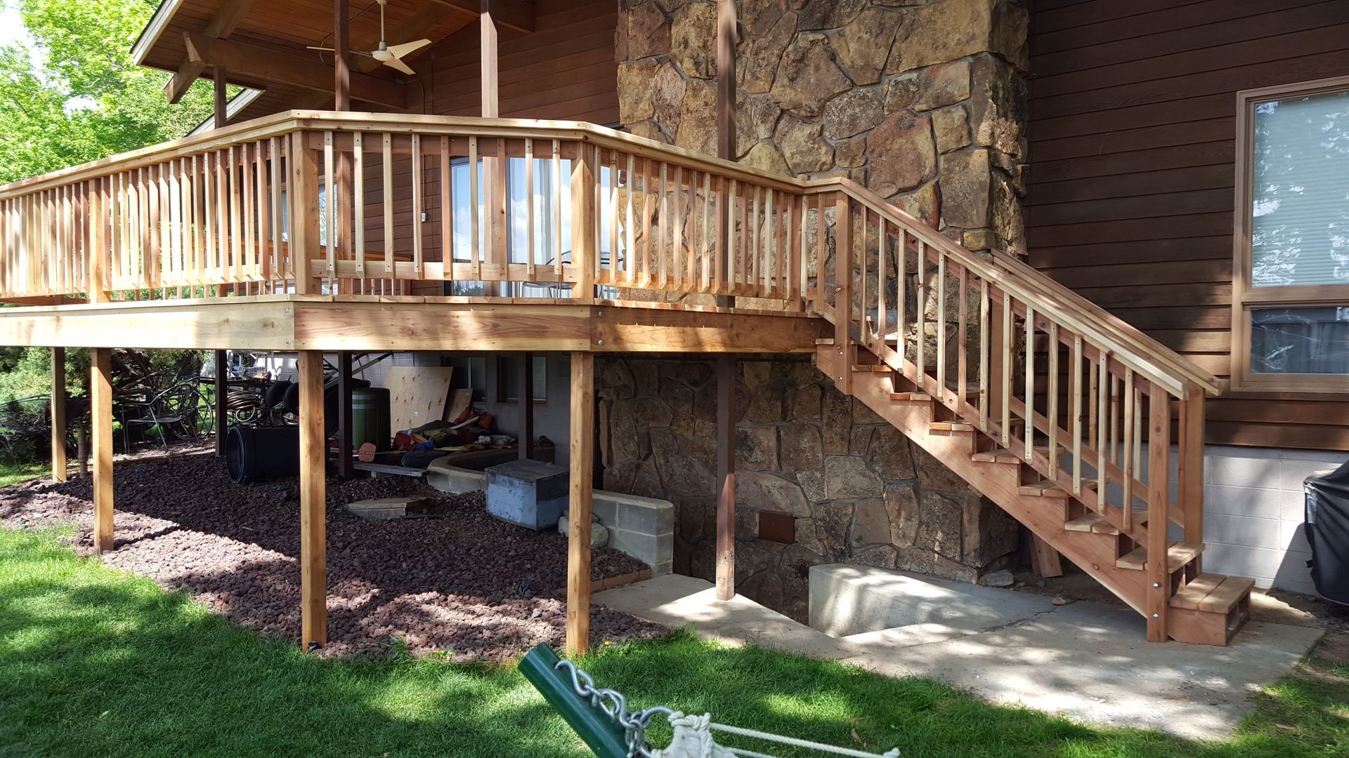Wooden raised deck with stairs attached to a brick house, shaded by trees and overlooking a yard.