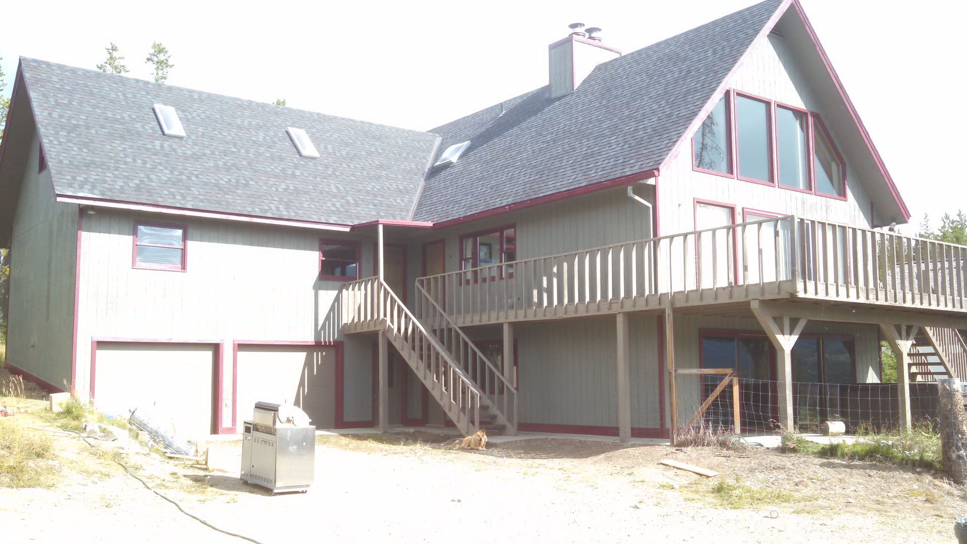 A house with a gray roof, white siding, and a wooden deck on a sunny day.