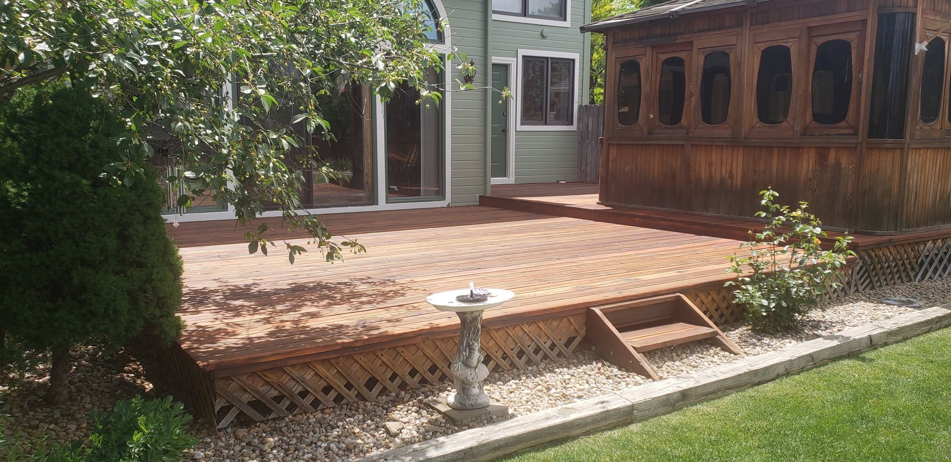 Backyard patio with brick pavers, wooden deck steps, and a small birdbath in the center.