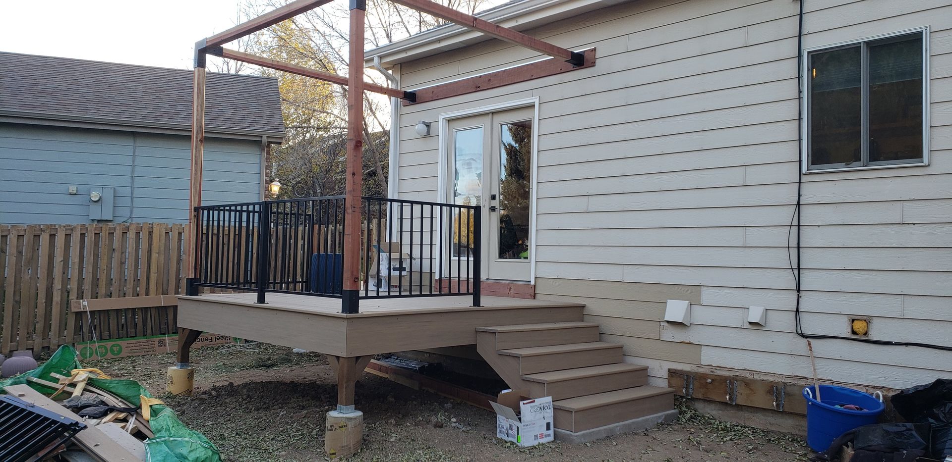 Backyard deck with stairs and pergola attached to a white house, with a door and window.