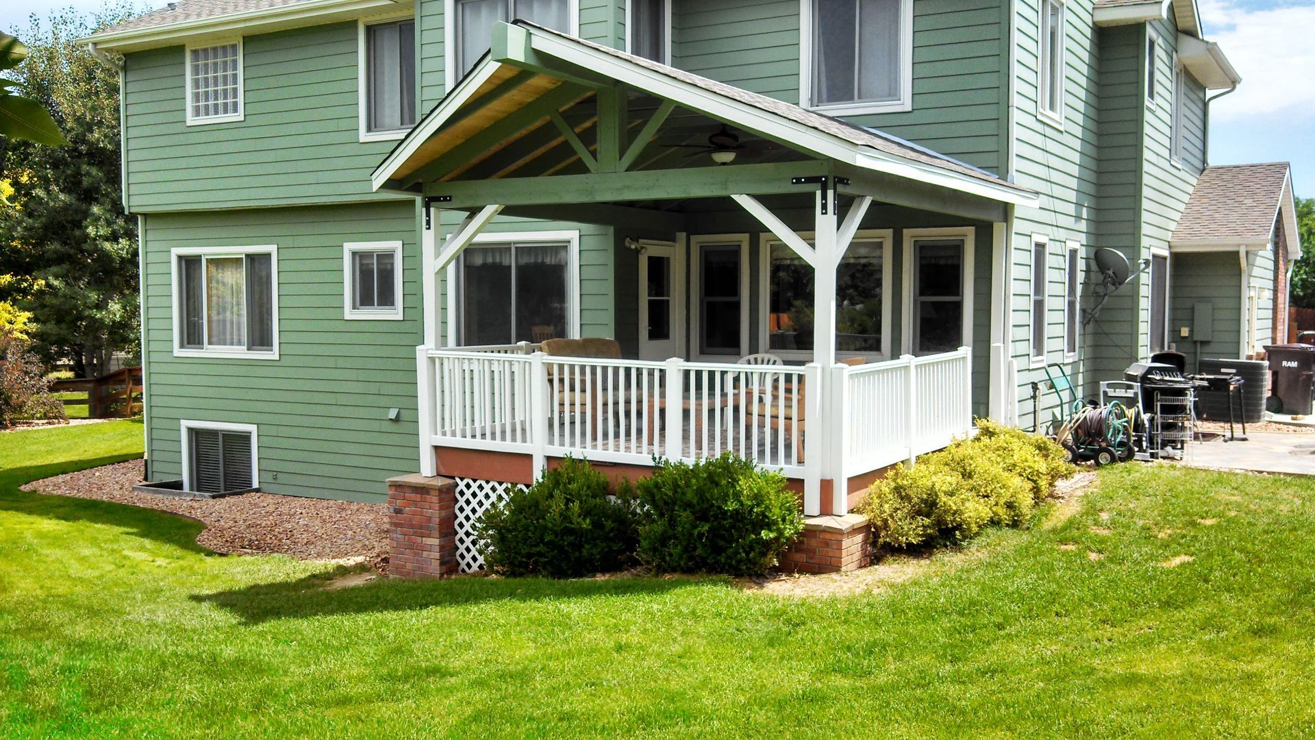 Green two-story house with a covered porch, white trim, and a small landscaped yard.