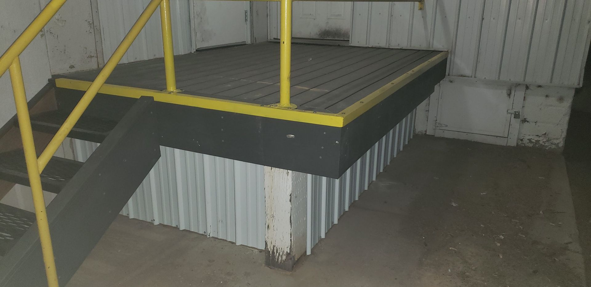 Industrial metal staircase with yellow railings and gray platform against a corrugated wall.