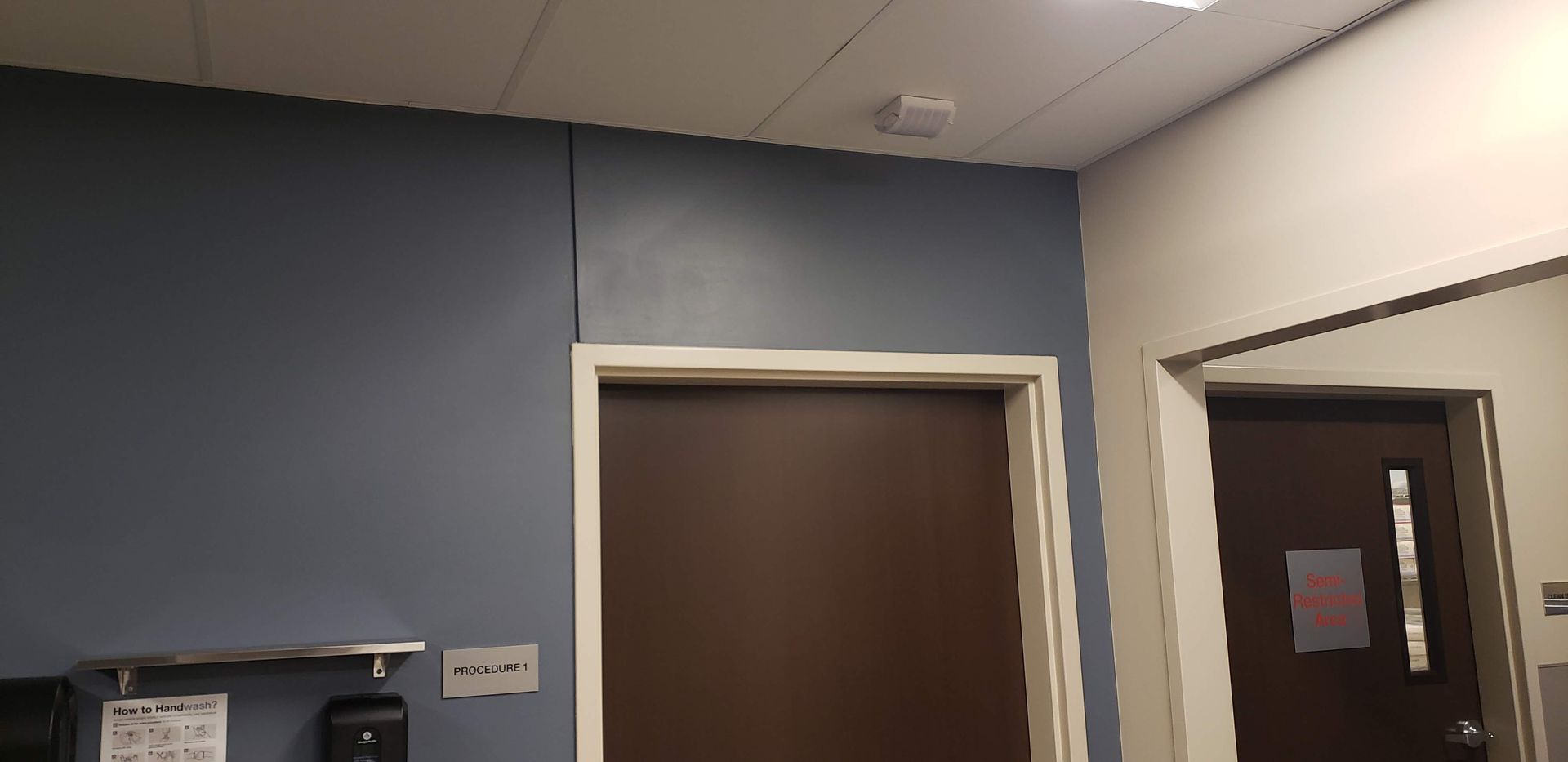 Hallway with blue and white walls, a brown door, and a doorway with a posted notice.