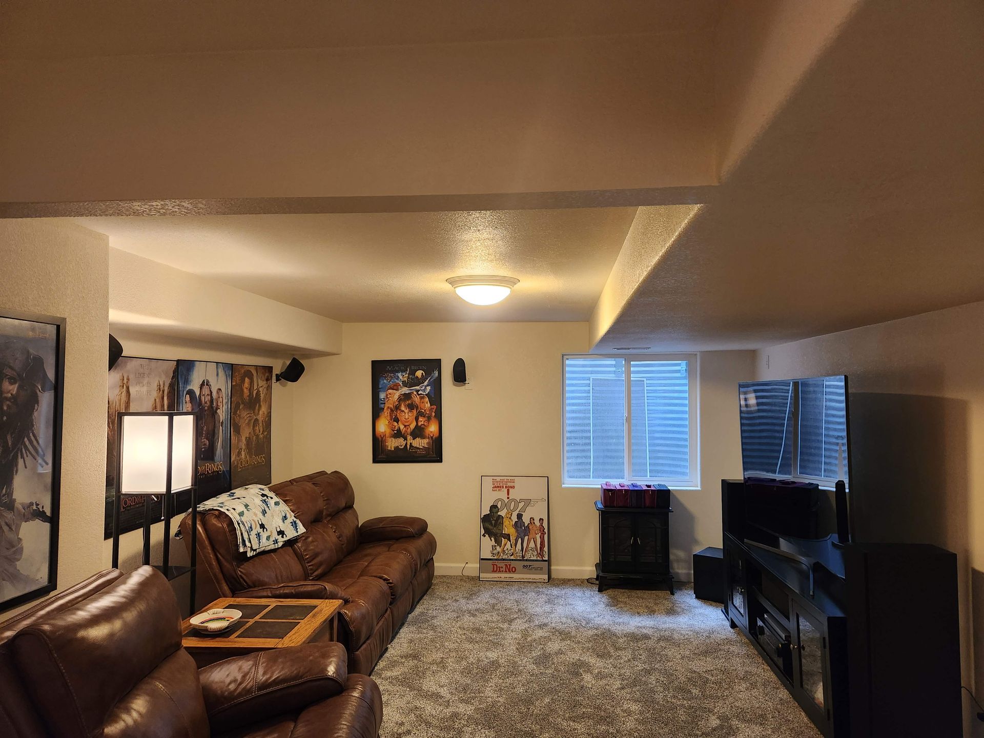 Living room with brown leather sofas, TV, patterned rug, and window blinds under warm ceiling light.