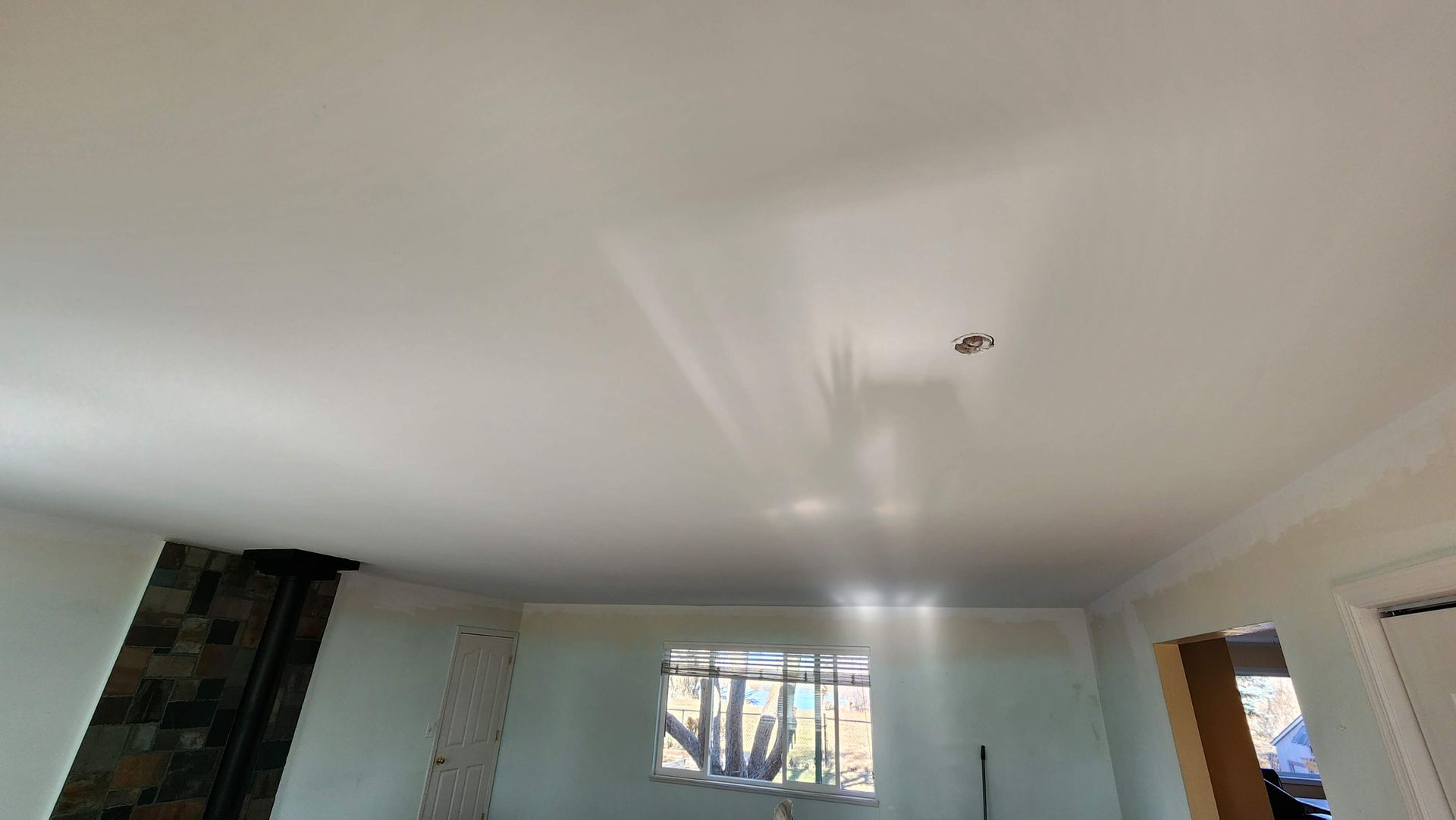 Empty room with white ceiling, light blue walls, a window, and sunlight reflecting on the ceiling.