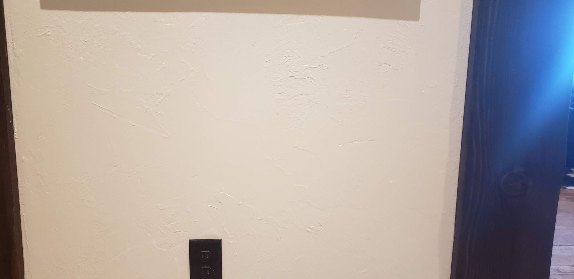 Plain white wall with a black outlet below and a bright blue-lit doorway on the right.