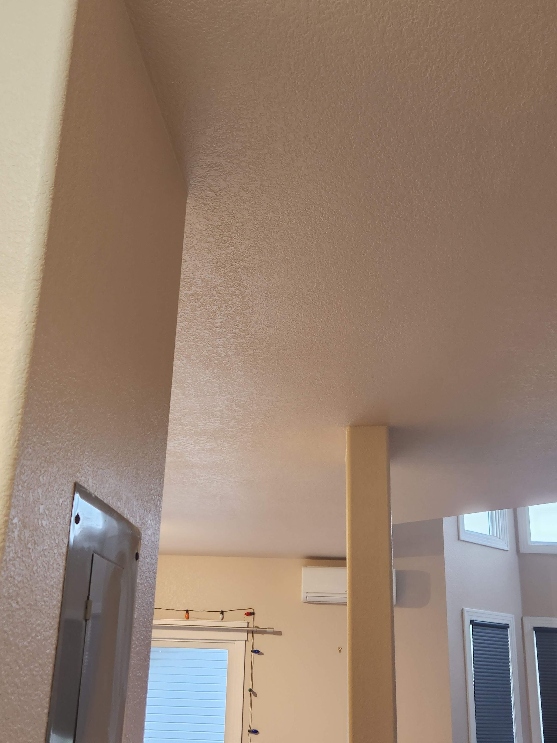 Interior hallway with textured white ceiling, beige walls, a column, and a wall-mounted air conditioner.