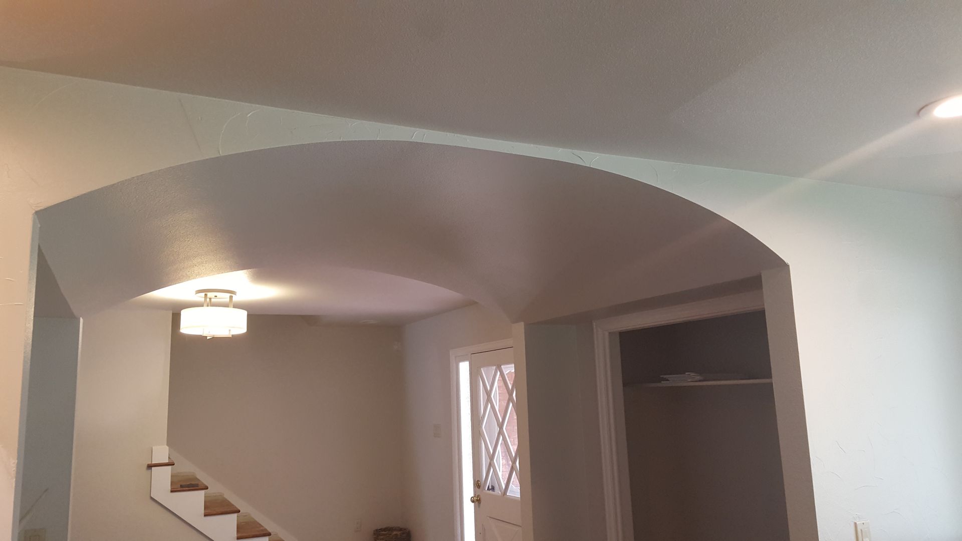 Living room with arched opening, staircase, ceiling light, and an open closet nook.