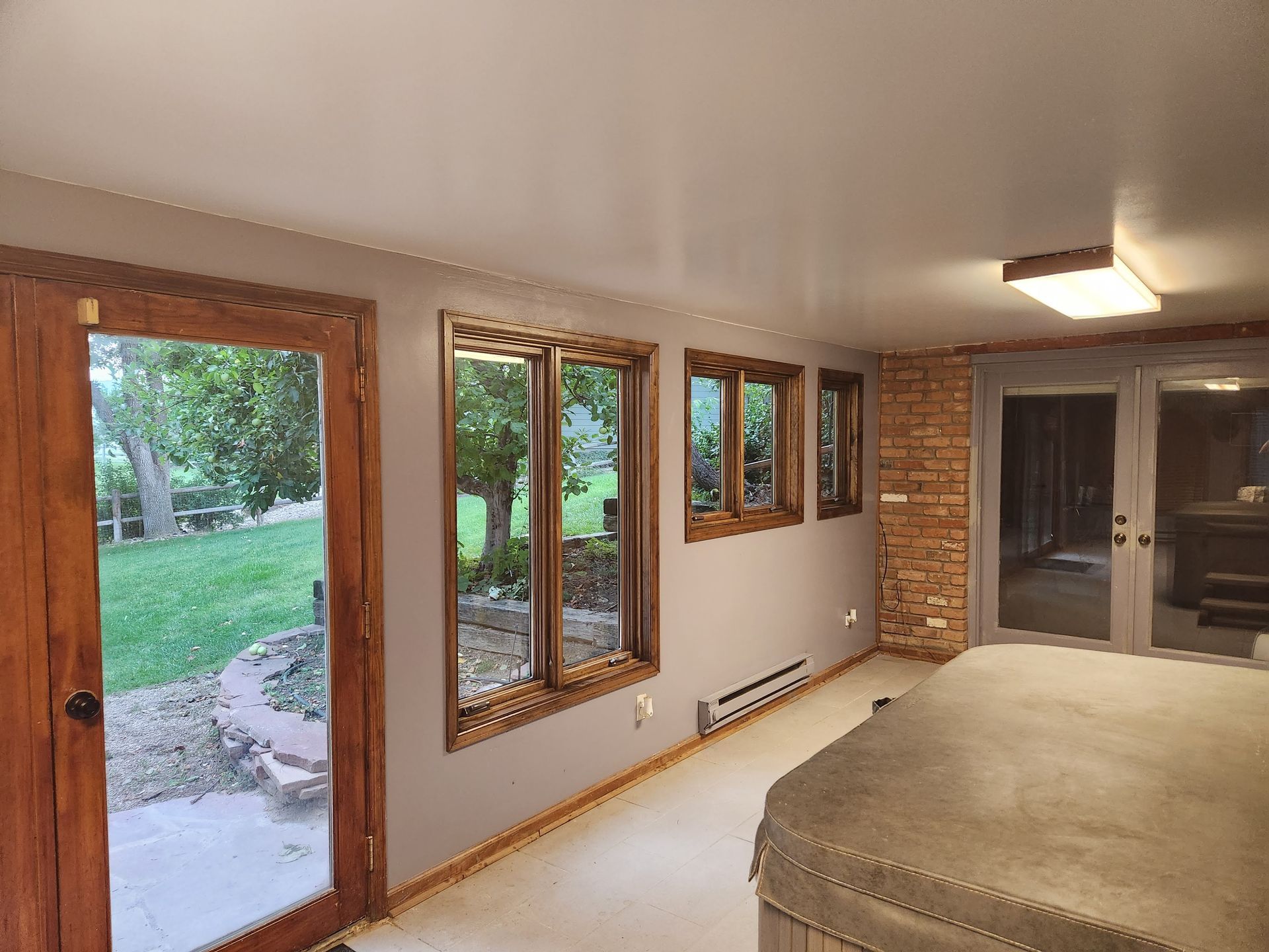 Bedroom with beige walls, wood-trimmed windows and door, and a view of a green backyard.
