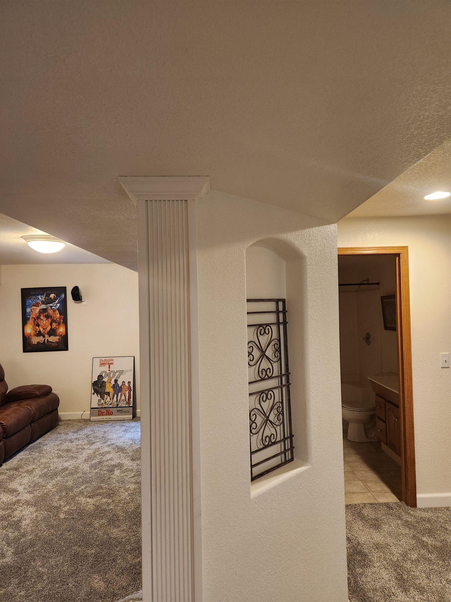 Living room with white column, carpet, brown sofa, framed art, and open doorway to a hallway.