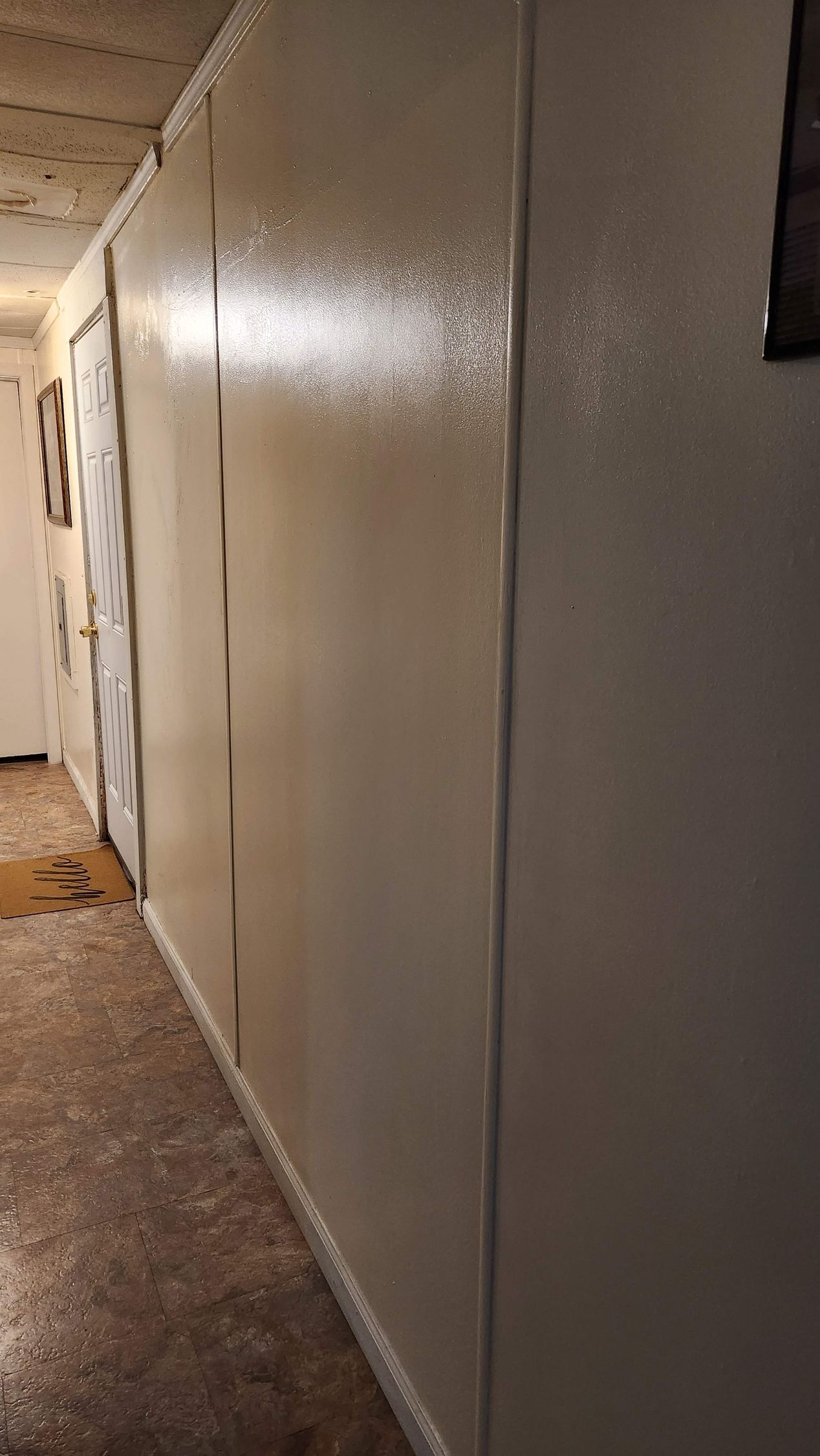 Long white wall panels in a dim corridor with a brown floor and ceiling lights.