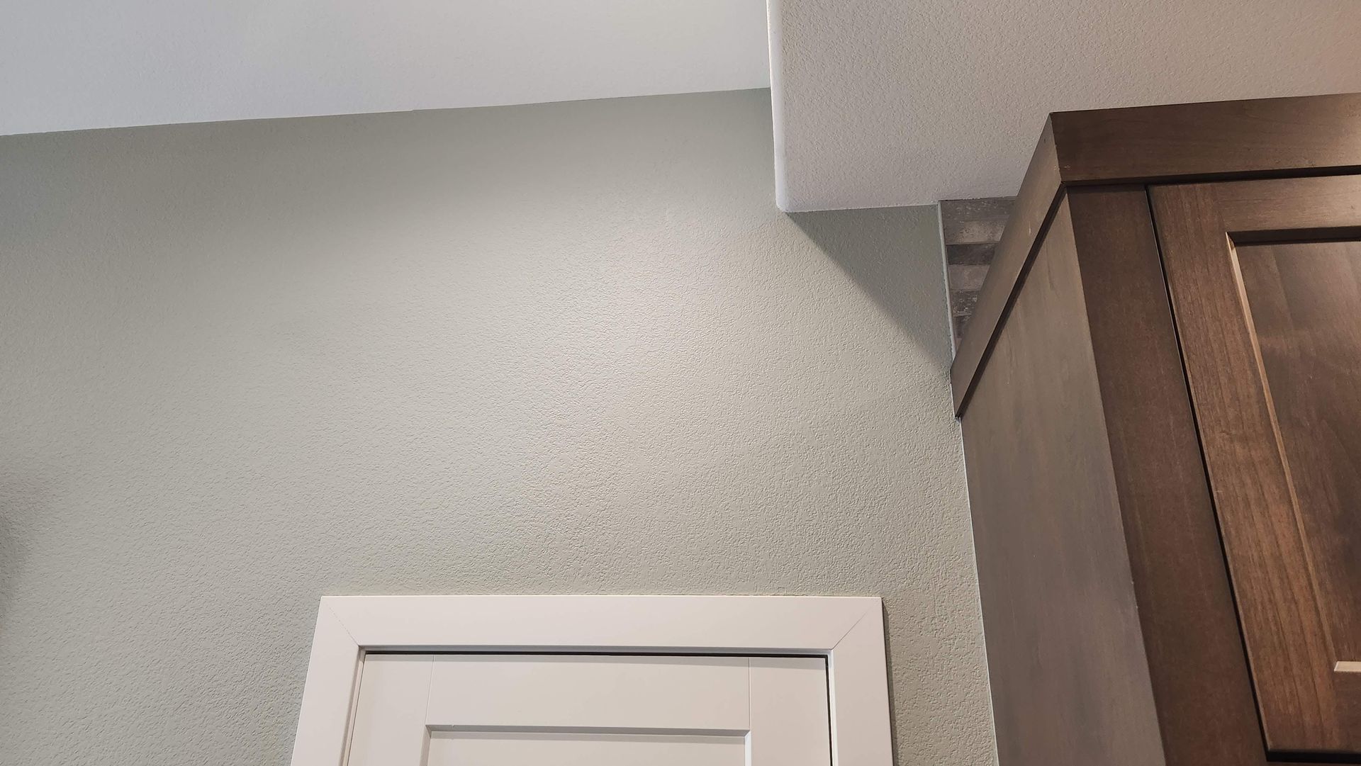 Gray wall above a white door frame beside a brown wooden cabinet in a home interior.