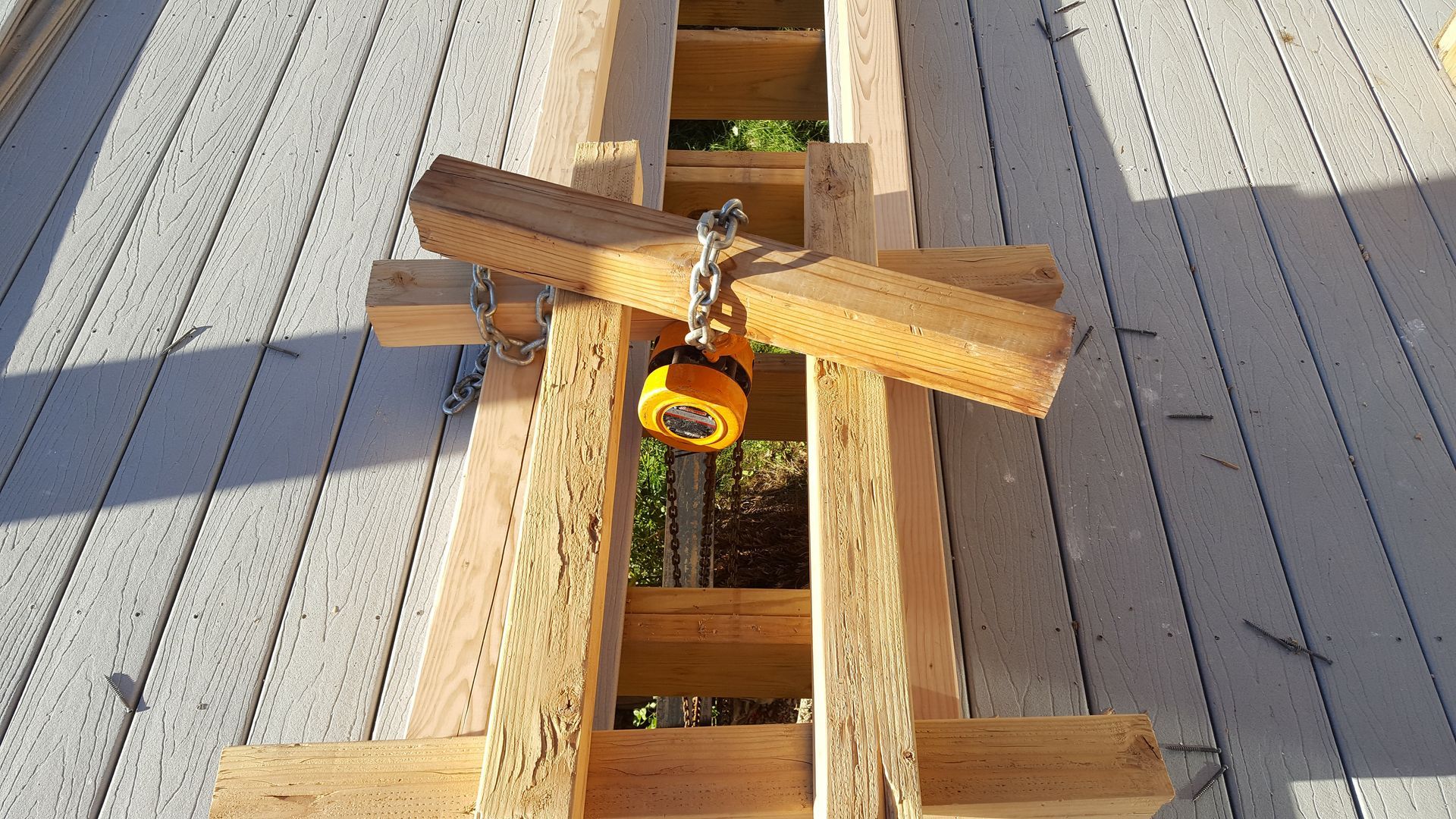 Wooden clamp and yellow padlock securing two boards on a sunlit deck gap.