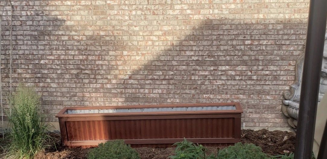 Wooden storage bench against a brick wall in a small landscaped outdoor area.