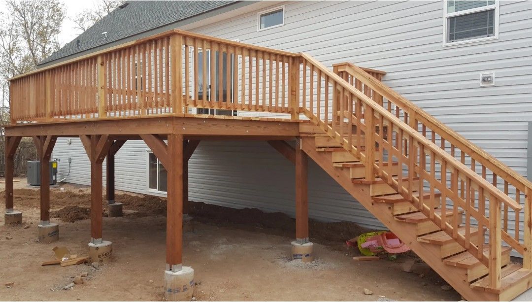 Raised wooden deck with railing and stairs attached to a house under construction