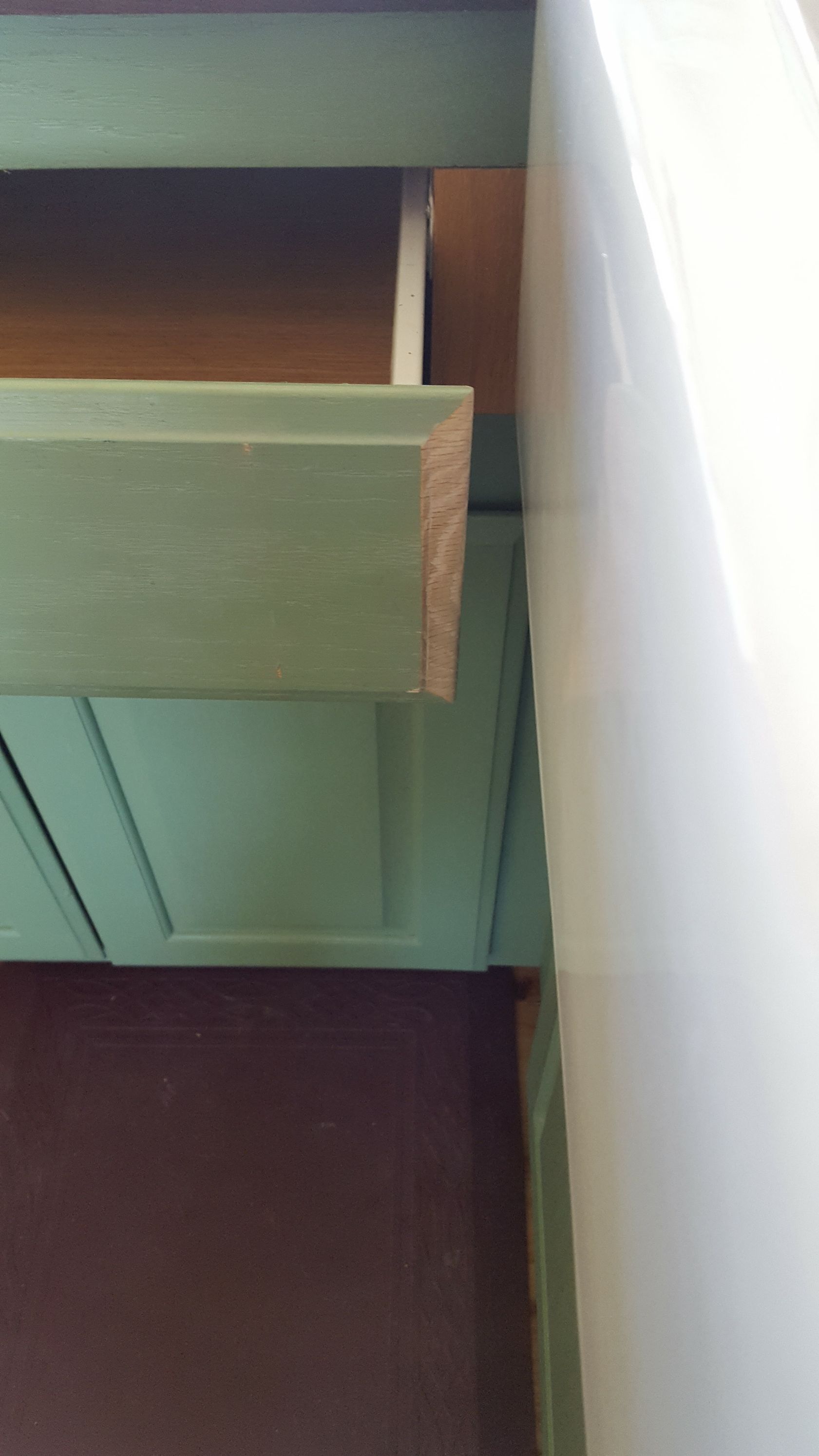 Close-up of a green cabinet drawer slightly open beside a white curtain and maroon floor.