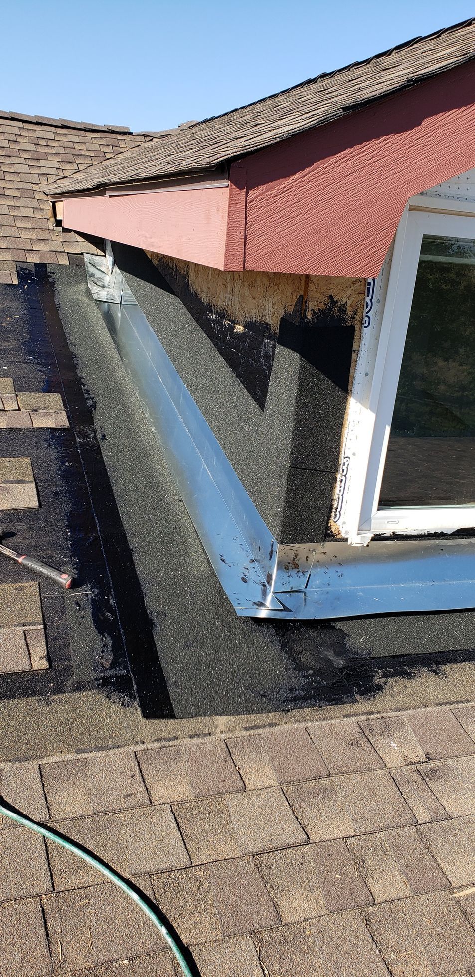 Damaged roof edge with bent blue flashing and peeling pink siding beside a window.