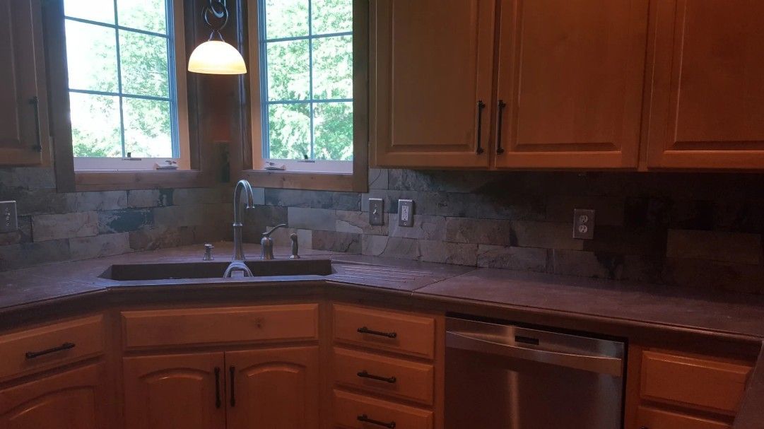 Warm kitchen with wooden cabinets, granite counters, sink under window, and hanging pendant light.