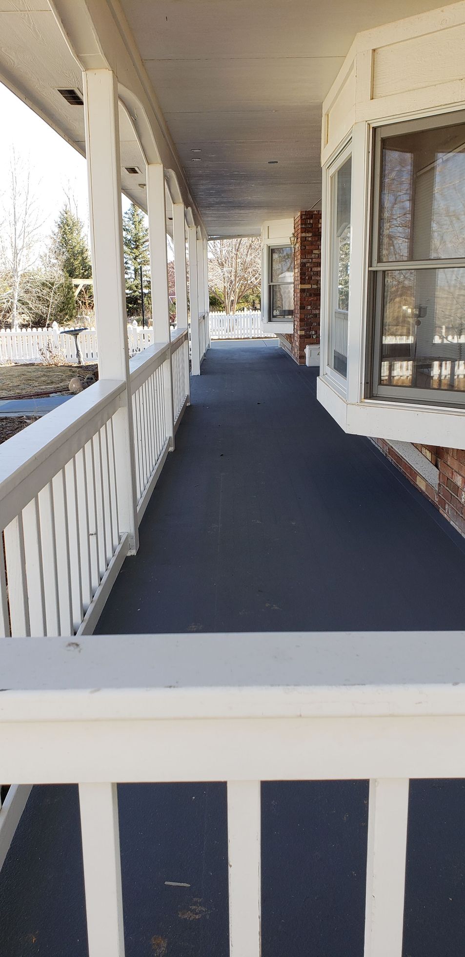 Covered porch walkway with white railings and posts beside a house.