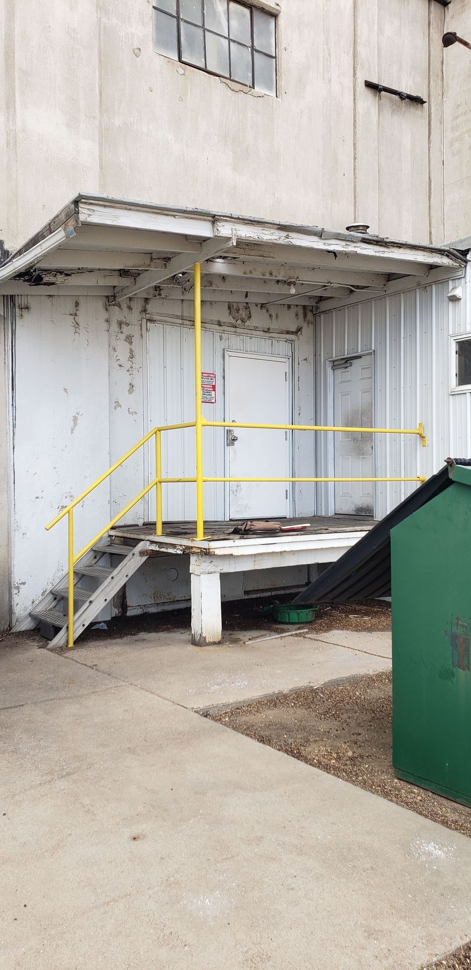 Exterior loading dock with yellow handrails, stairs, and a concrete ramp beside a white building.