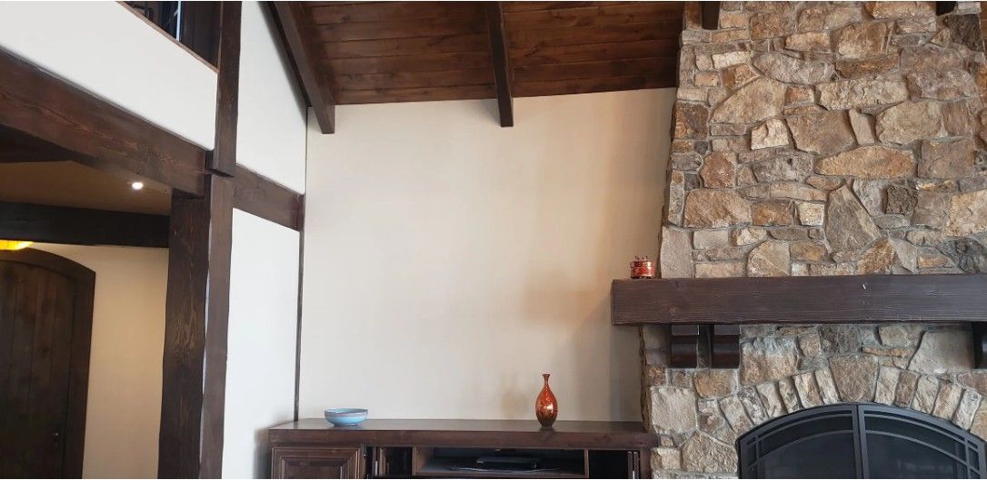 Rustic living room with stone fireplace, wooden beams, white walls, and a small table with a vase.