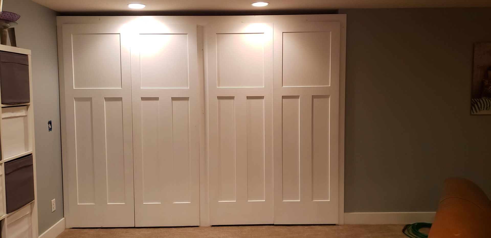 Wall with four white closet doors under ceiling lights in a beige room.