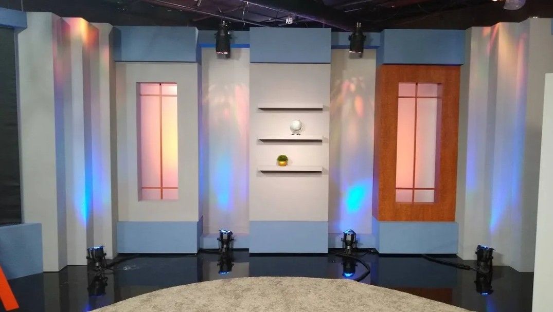 Modern stage set with white panels, pink-lit windows, orange door, and blue accent lights.
