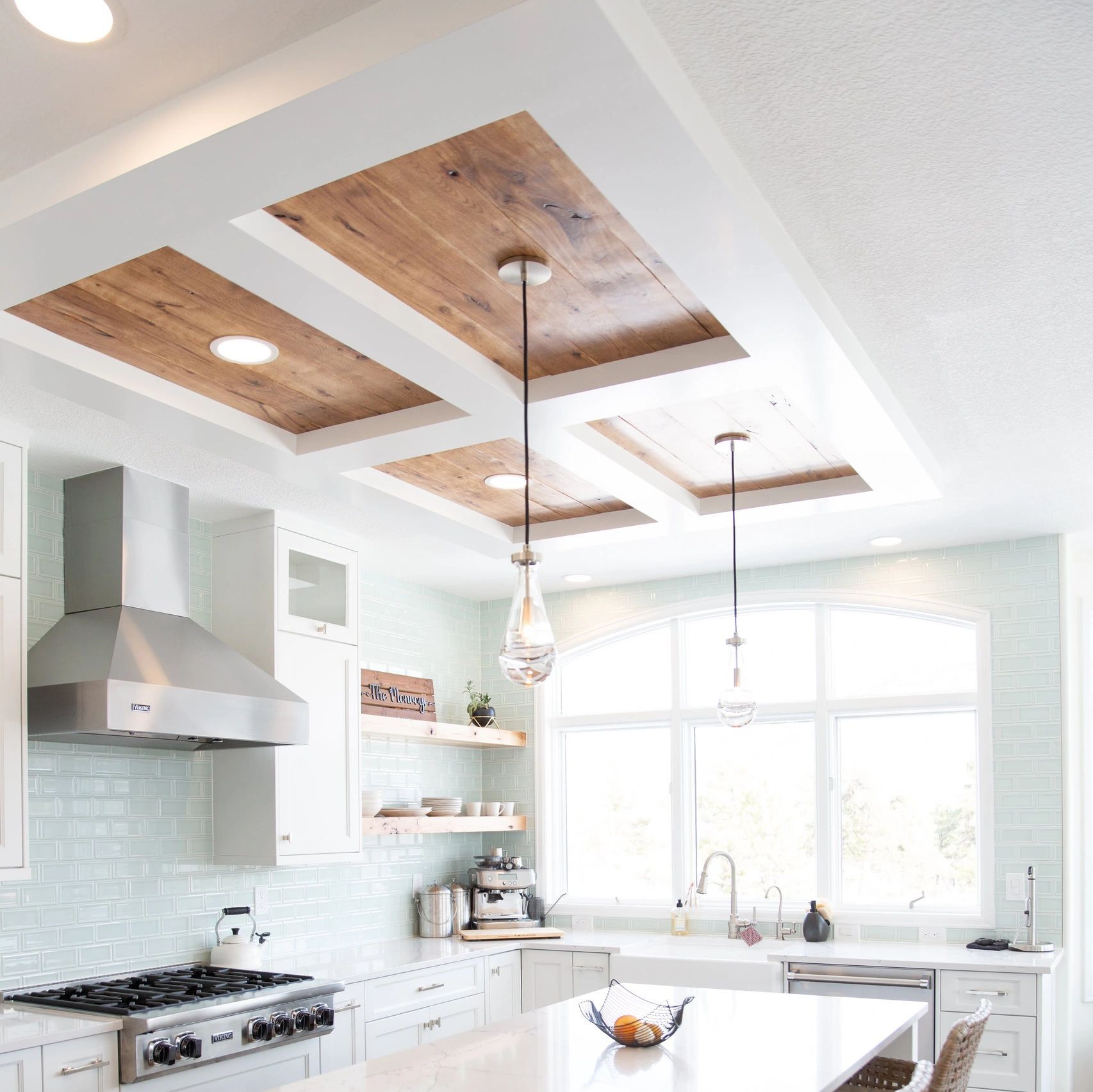 Bright white modern kitchen with skylights, stainless stove, pendant lights, and a large island.