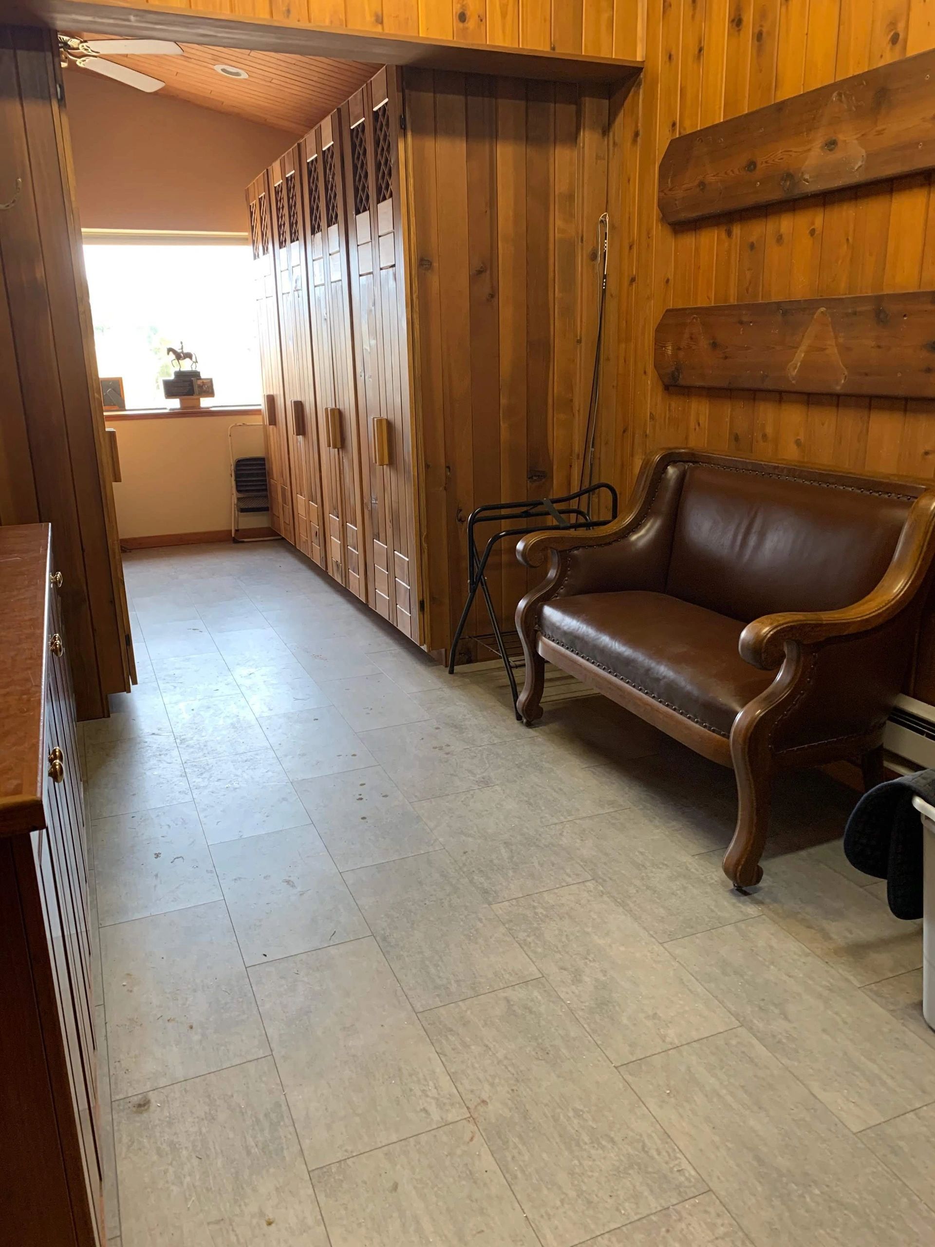 Empty hallway with a brown leather loveseat, wood cabinetry, and a beige tiled floor.