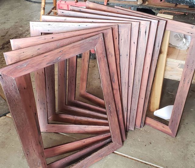 Stack of unfinished wooden picture frames leaning in a workshop or storage area.