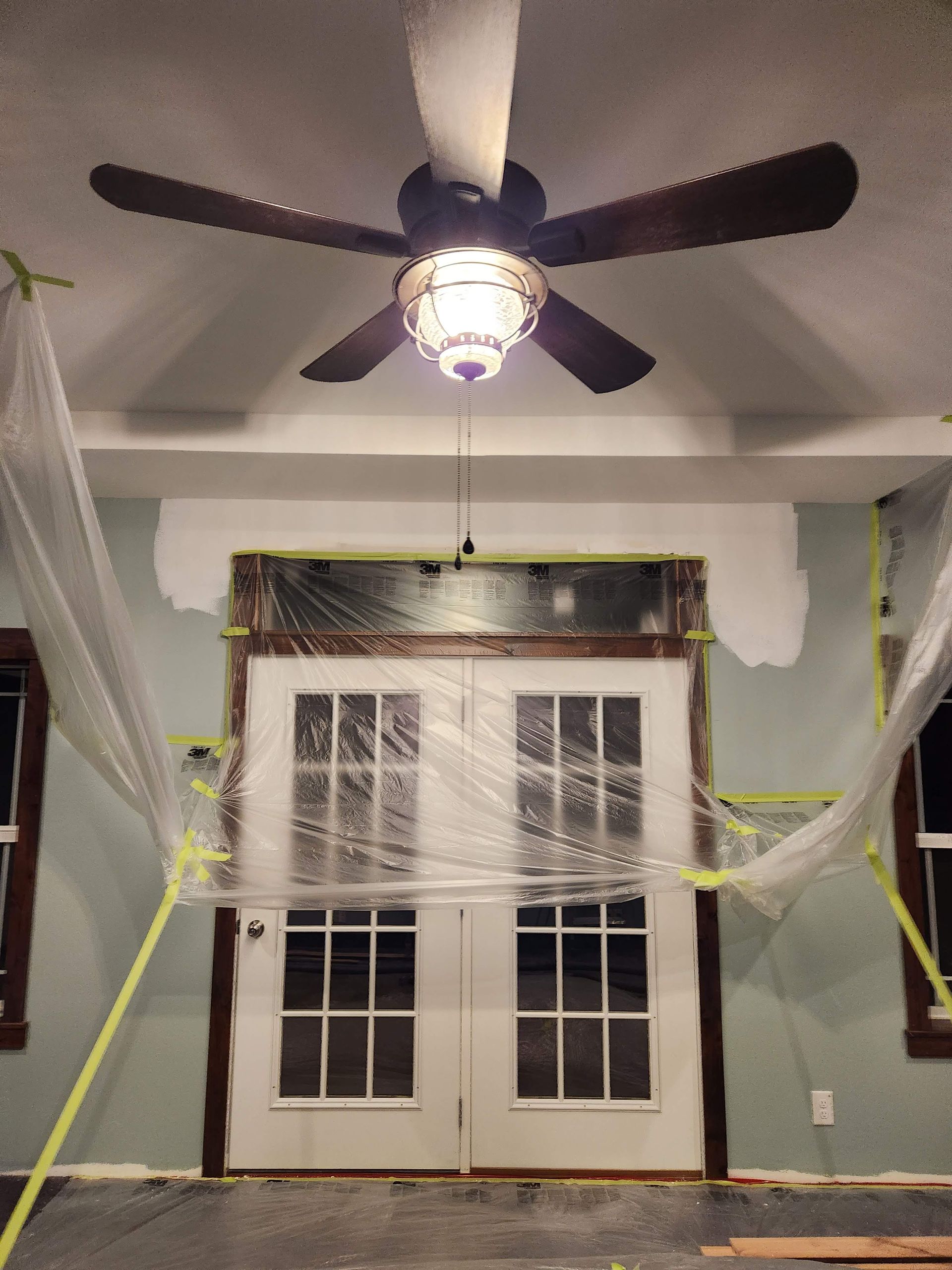 Living room with a ceiling fan, double doors, and Halloween-style white cobweb decorations on the walls and doors.
