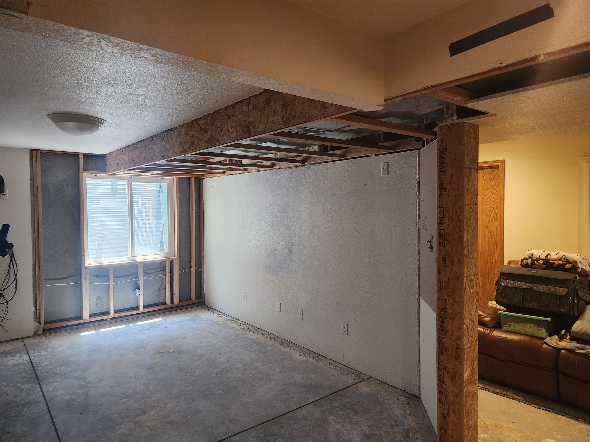 Partially demolished living room with exposed ceiling beams, bare walls, and a window at the far end.