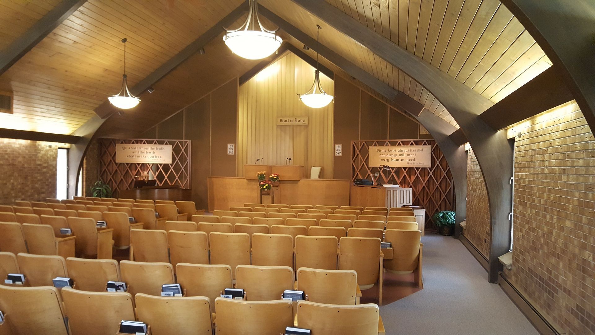 Wood-paneled auditorium with rows of tan seats and pendant lights under a vaulted ceiling.