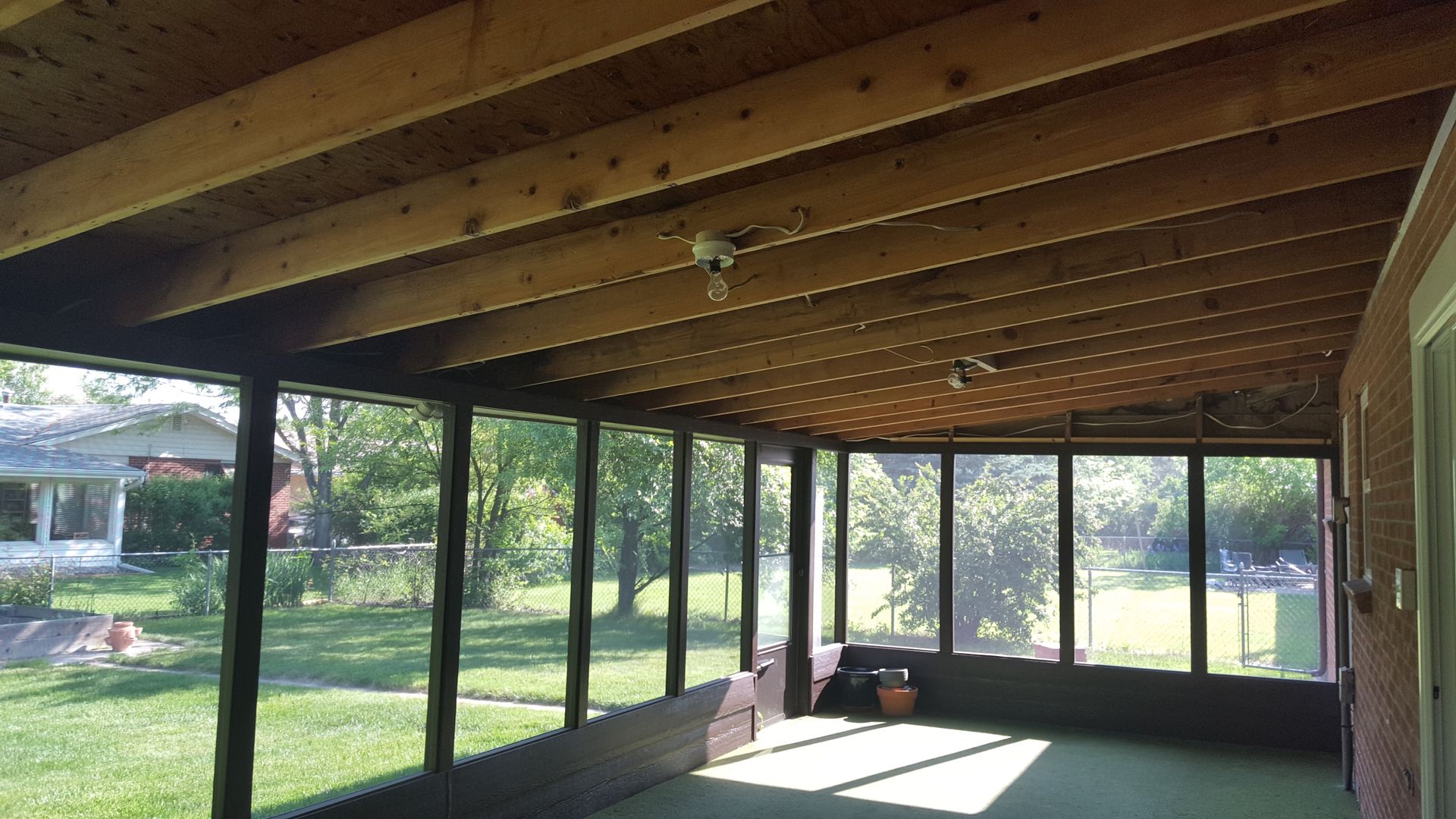 Covered porch with wood ceiling, screened windows, and a sunlit view of a grassy backyard.