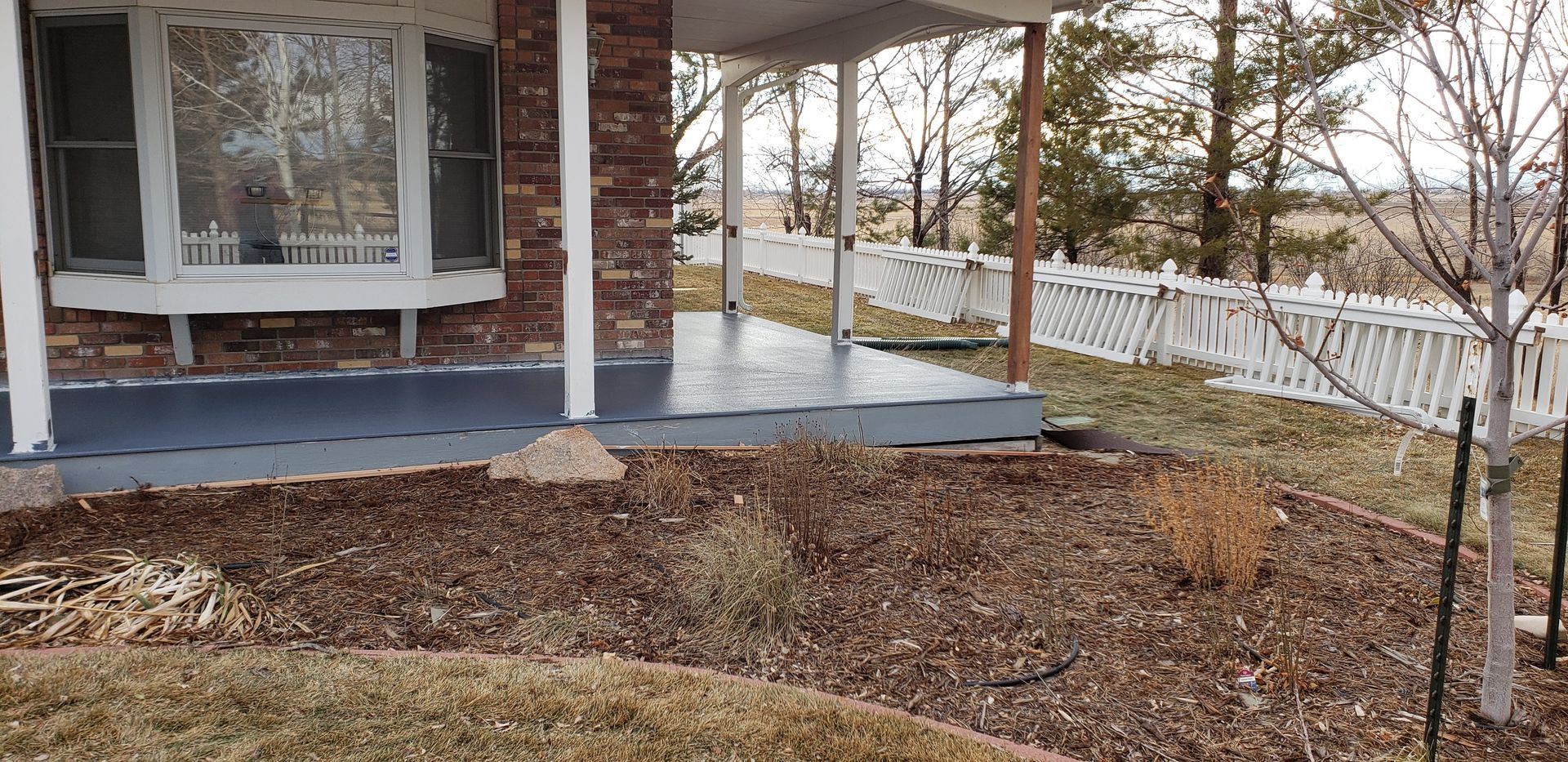 Front porch of a house with white columns, a bay window, and a winter yard with white fence and bare trees.
