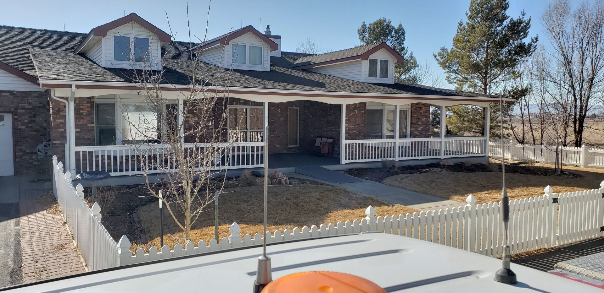 Two-story house with a covered porch and white fence on a sunny day.