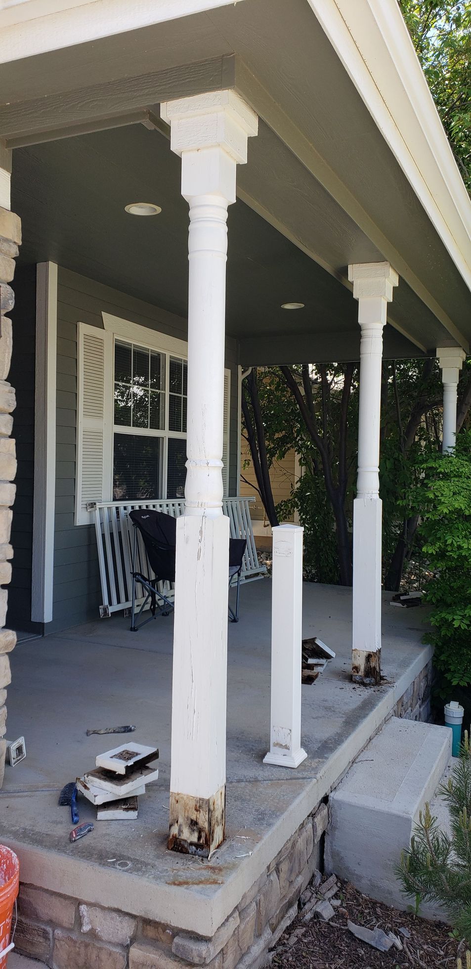 Front porch under construction with white columns, stacked chairs, and tools on the concrete floor.
